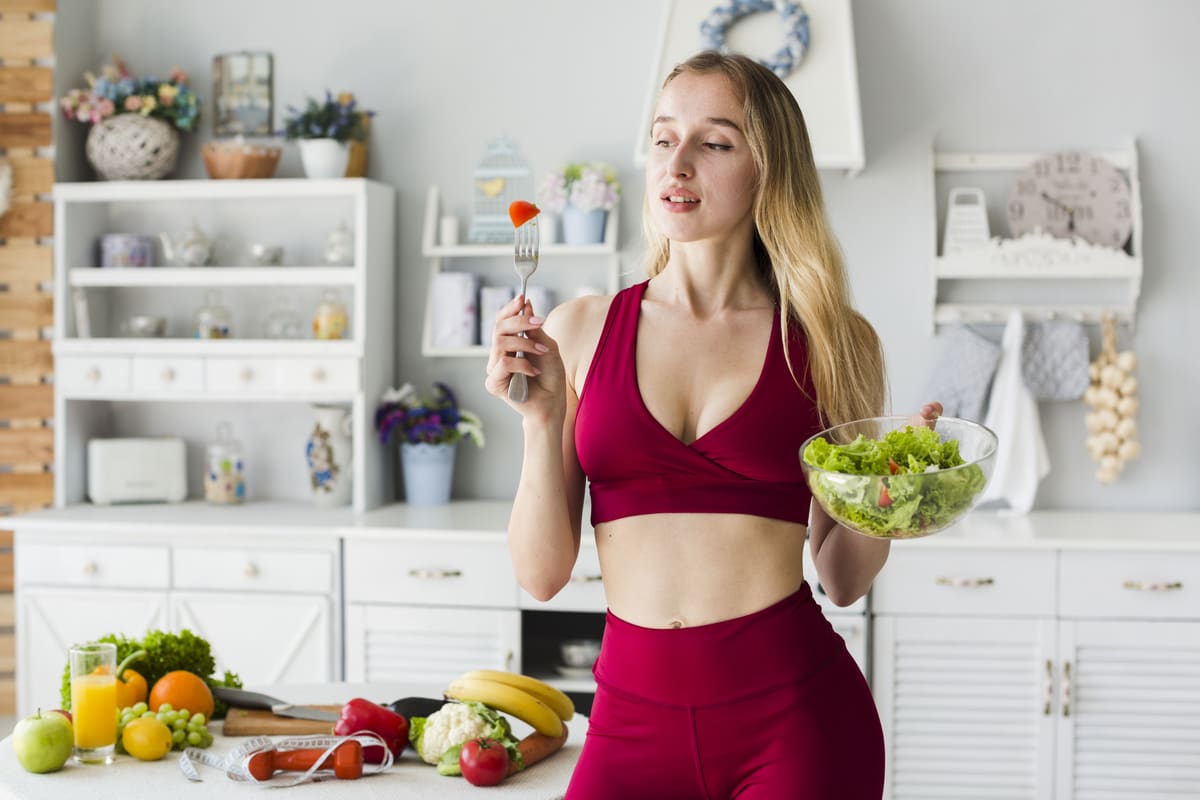 ragazza in cucina con una ciotola di insalata e una forchetta in mano
