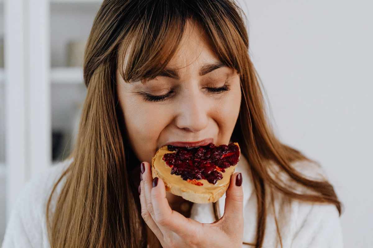 Donna che addenta una fetta di pane con marmellata
